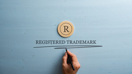 Letter R cut into wooden cut circle and male hand writing a Registered trademark sign under it - 530488761