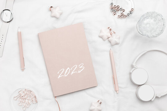 New Year planning concept, female work, pink diary for year 2023, pen, christmas toys, headphones, watch on white bed textile background. Woman lifestyle working place, new goals, beginnings
