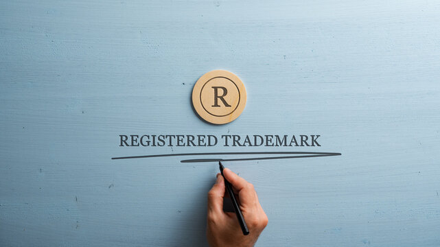 Letter R cut into wooden cut circle and male hand writing a Registered trademark sign under it