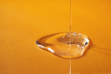 A drop of body gel or shampoo pouring from above on a yellow saturated background.