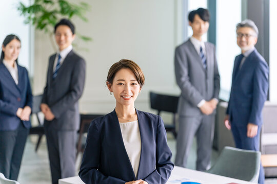 オフィスに立つ女性リーダーとサポートするビジネスパーソンのグループ