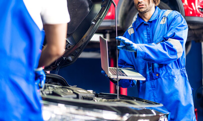 Professional car technician mechanic team in uniform use laptop work fixing vehicle car engine and maintenance repairing checking under the car in auto service. Automobile service garage