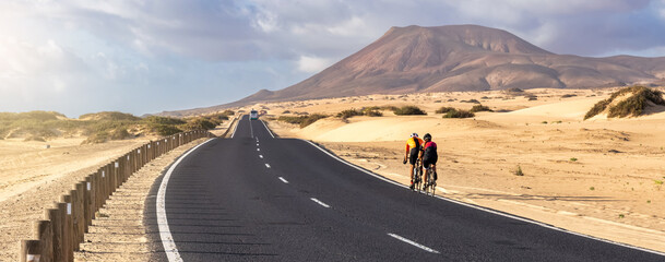 two cyclists cycling on a sunny day in a road of the Corralejo dunes in Fuerteventura, Spain