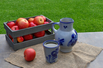 Äpfel und ein Krug Apfelwein auf einem Tisch im Garten.