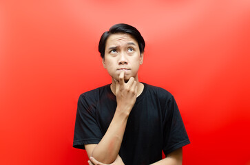 a young asian man in black t-shirt thinking and wondering with hand gesture isolated on red.