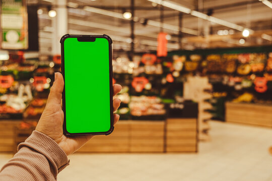 Mobile Phone Chroma Key. Close Up Of Woman Hand Holds Smart Phone With Green Screen At Shopping Mall Store. Buying Food At Supermarket, Grocery Shop Center Online. Department Store. Gadgets