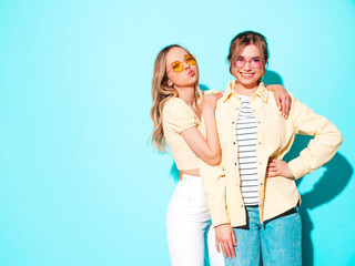 Two young beautiful blond smiling hipster girls in trendy summer hipster jeans clothes. Sexy carefree women posing near wall. Trendy and positive models having fun
