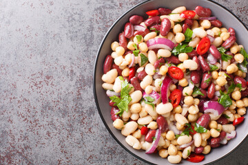 Delicious vegetable salad three beans with chili peppers and red onions close-up in a bowl on the table. Horizontal top view from above