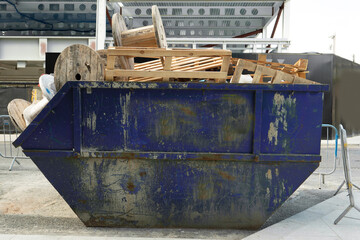 Green metal skip full of construction site rubbish and electric cable reels ready for collection in...