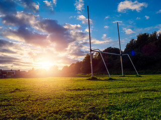 Small tall goal post on training field for rugby and Irish national games hurling, camogie, Gaelic football and soccer at sunset. Rich green and blue colors. Sun flare and blue sky. Sport area - obrazy, fototapety, plakaty