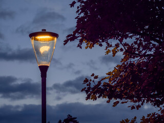 Old style lamp with modern energy efficient LED light in a street at dusk. Blue sky in the background. Mixing old and new technology. Warm color lantern in a street.