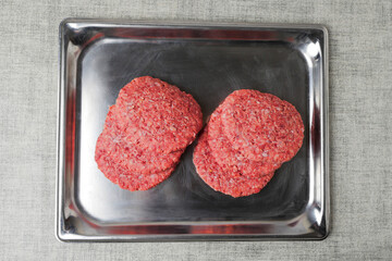 Stack of fresh uncooked beef burgers on a stainless steel metal tray and on a simple table cloth. Meat industry product for mass consumption.