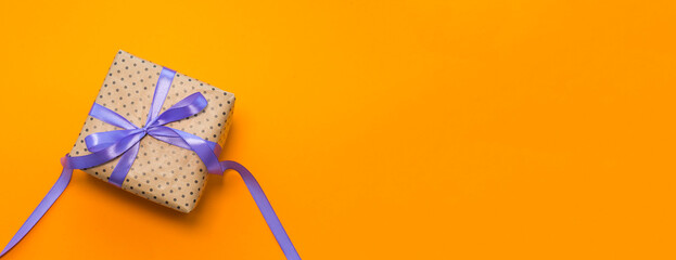 A gift wrapped in craft paper, tied with a purple ribbon on an orange background
