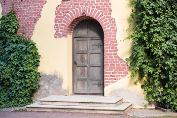 An ancient wooden door with steps with ivy of an abandoned tower or house.