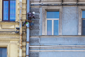 An industrial climber is hanging high on a rope and painting the facade of a building. The concept of industrial mountaineering.