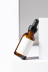 Amber glass dropper bottle with black pipette and whita label on white podium.Beauty Cometic...