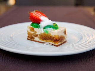 Delicious fig mousse cake slice with white chocolate cream and strawberry on top on wooden table background. Restaurant menu and confectionery concept. Close-up. Copy space.