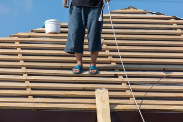 Workers install metal roofing on the wooden roof of a house.
