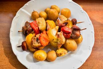 Skewer with piece of pork meat, paprika, sausage and onion, boiled potato plate.