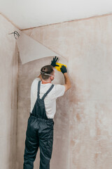 Male worker in coveralls applying fiberglass surface tissue on the wall