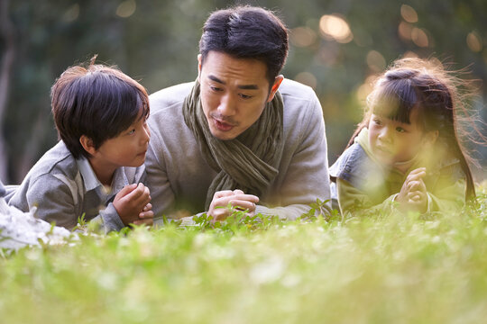asian father and two children relaxing outdoors in city park