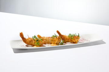 Traditional greek appetizer - kataifi wrapped shrimps on white plate. Crispy shrimp in kataifi crust in summer day. Shrimp appetizer fried in kataifi dough. Crispy prawns in modern style.