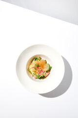 Elegant salad with crab meat, espuma sauce and lettuce on white table with harsh shadows. Green salad with crab and creamy sauce in summer menu. Aesthetic food. Seafood appetizer.