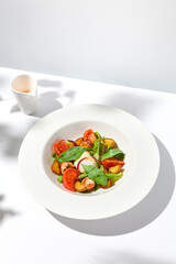 Salad with octopus, baked potatoes and poached egg on white table with hard shadows. Seafood salad with vegetables and potatoes in summer menu restaurant. Octopus and eggs salad in modern style.