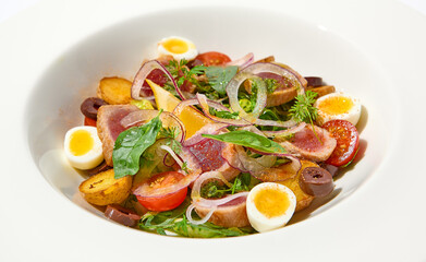 Traditional french salad nicoise with tuna, potatoes, eggs and vegetables on white table with harsh shadows. Tuna salad with quail eggs on white background with shadows of leaves.