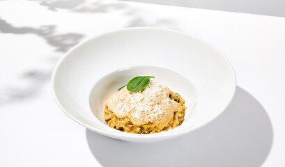 Italian food - mushrooms risotto with creamy espuma on light background. Mushroom risotto with cheese in summer menu Italian risotto with hard shadows from tree leaves. Trendy menu concept