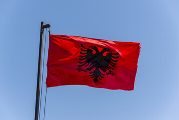 Albania flag. Albanian flag on a flagpole waving on a bright blue sky background. - 530515103