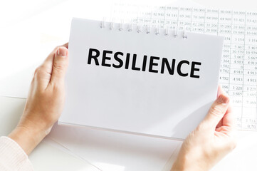 RESILIENCE inscription on a sheet of notepad in the hands of a businessman at an office desk, a business concept