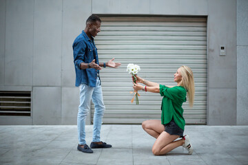 Blondie woman kneeling giving flowers to an african man