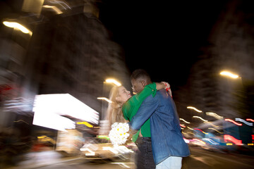 Multiethnic couple embracing in the street at night