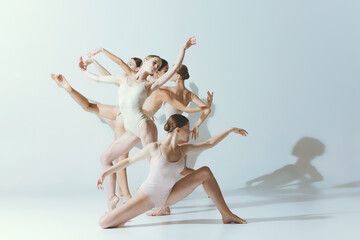 Group of young women, ballerinas dancing, performing isolated over grey studio background. Tender beauty of youth