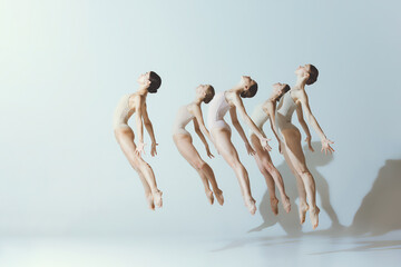 Group of young girls, ballet dancers performing, posing isolated over grey studio background. Jump...