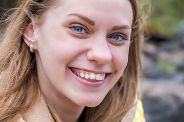 Fototapeta premium Portrait of young attractive blue-eyed woman looking at camera and smiling in yellow jacket. Selective focus