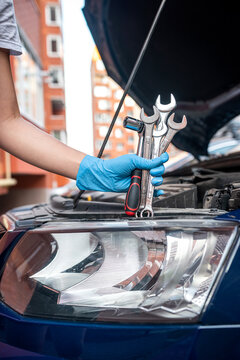 Close-up of car mechanic's hand holding wrench to remove part in engine compartment of car.
