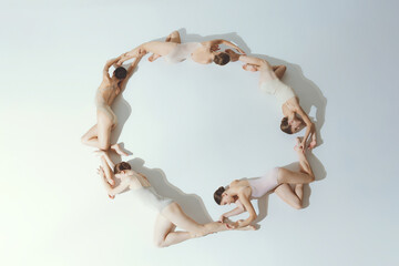 Group of young girls, ballet dancers performing, posing on floor isolated over grey studio background. Making circle