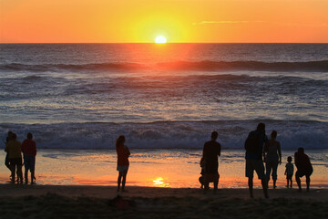 Des personnes observant le coucher de soleil face à la mer