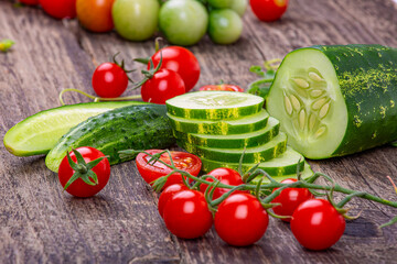 Sliced cucumbers and tomatoes on a branch on an old wooden background