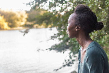 Portrait of afro american  young black woman looking at the horizon in in a relaxing, peaceful environment in nature. Female on the river bank. Copy space. Positive expression.