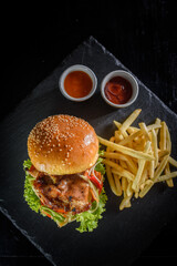 delicious grilled chicken burger and fries on black wooden table background