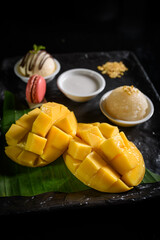 Mango sticky rice, coconut milk, ice cream and macarons on a black plate Popular Thai desserts in summer