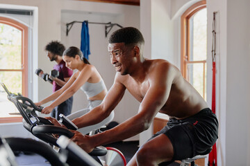 Fototapeta na wymiar Group of multiracial young adults doing cardio on exercise bike at the gym