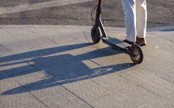 A man stands next to his electrical scooter at a pedestrian crosswalk. Eco way to comute in the crowded cities. Concept photo for e-scooter transportation