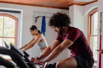 Young middle eastern man and biracial woman cycling on exercise bike at the gym