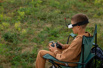 Child is sitting on a chair with remote control sticks, vr glasses of and fly on FPV drone at drone racing competition.