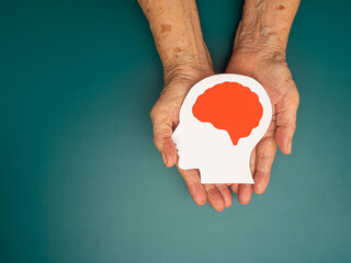 Top view of head with a brain made from paper on the palm senior woman over a green background