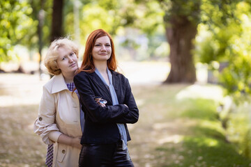 Fototapeta premium Two women together - blonde in light and redhead in dark clothes posing in a park. Cosplay - female version of Angel and Demon (Good Omens)